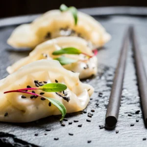 Dumplings with black sesame seeds on a black plate with chopsticks