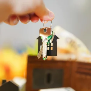 A key ring with a house key chain is held up by a hand